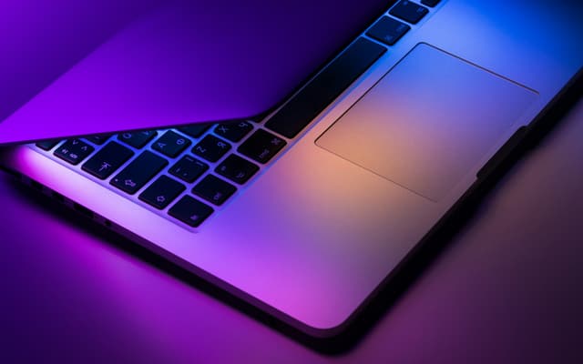 A laptop keyboard lit in purple and orange light
