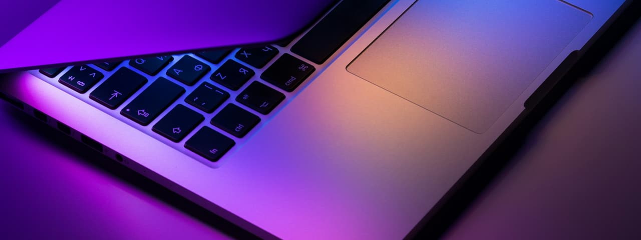A laptop keyboard lit in purple and orange light